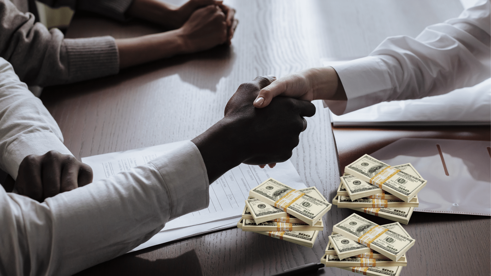 black and white hands locked in a handshake over a table with wads of money